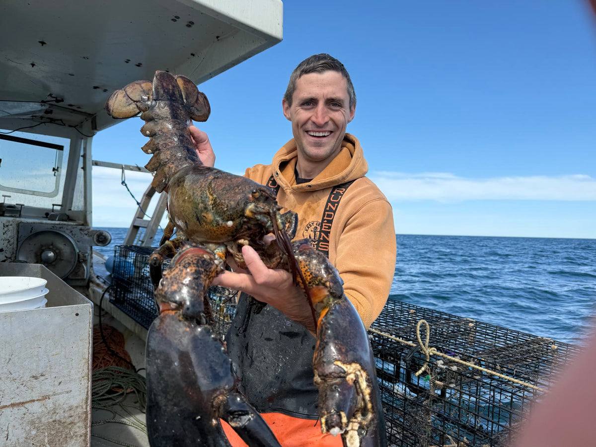 Jacob on deck holding a large lobster, traps and open water behind him