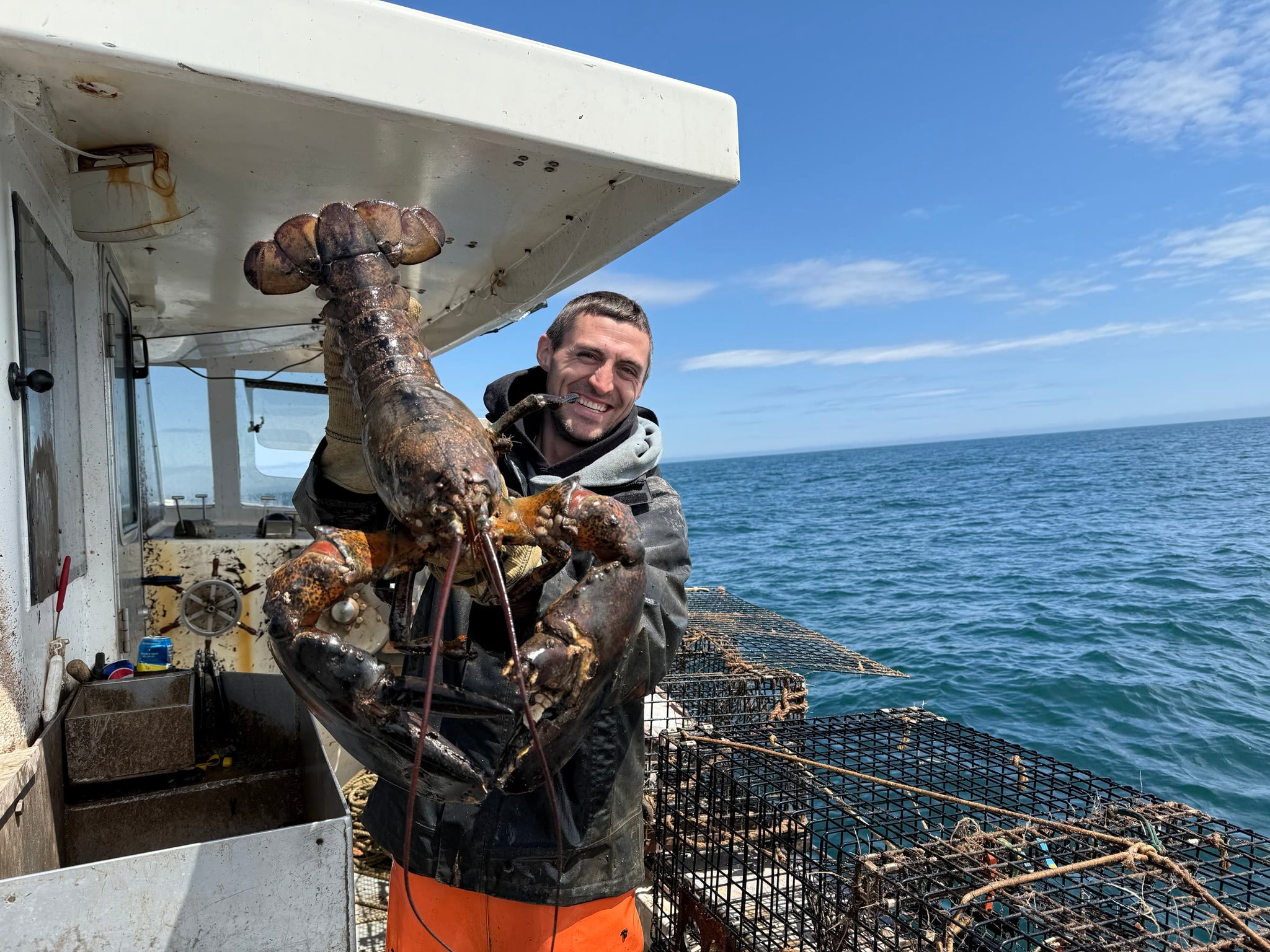 Jacob on deck holding a barnacled lobster, traps and open water behind him